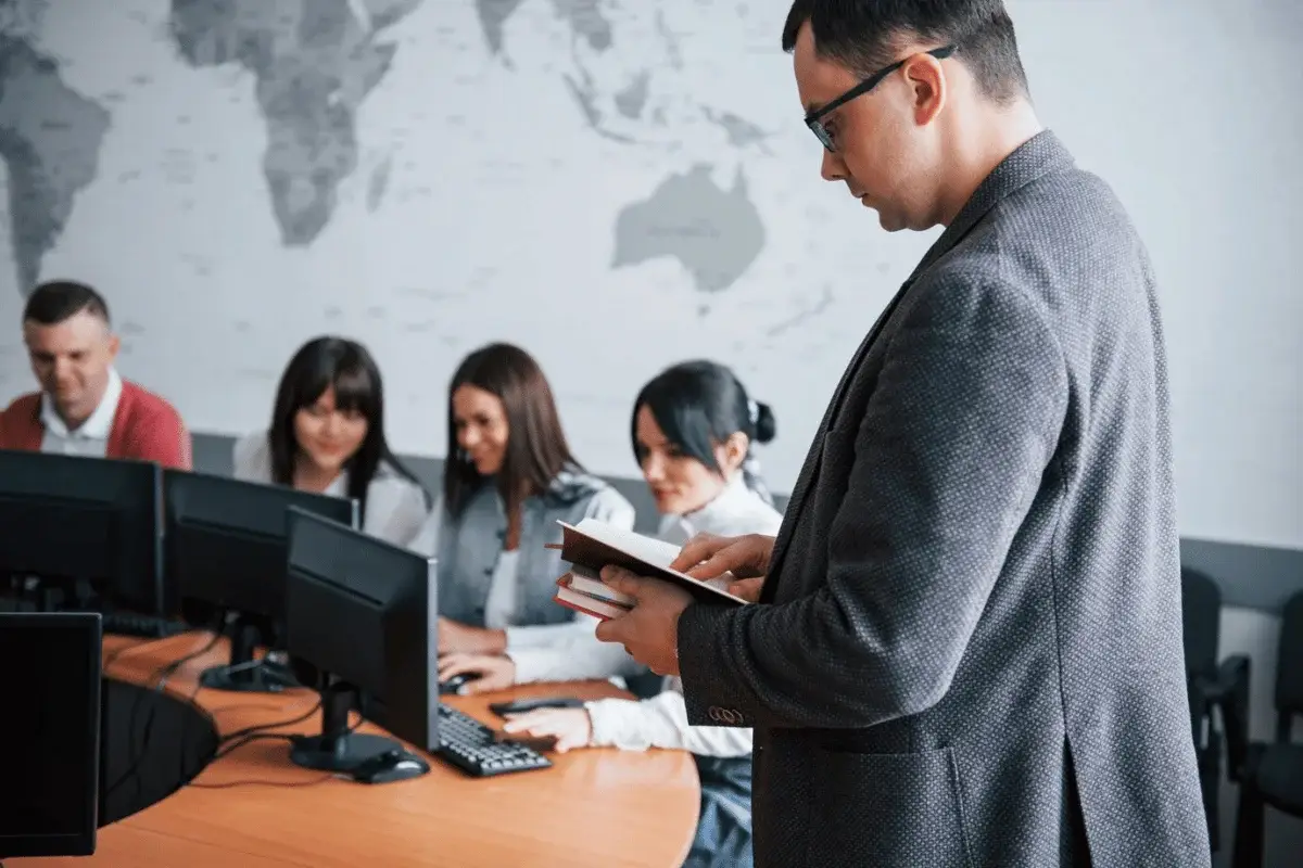 A professional giving instructions to a team in a modern office with multiple computers on the desk.