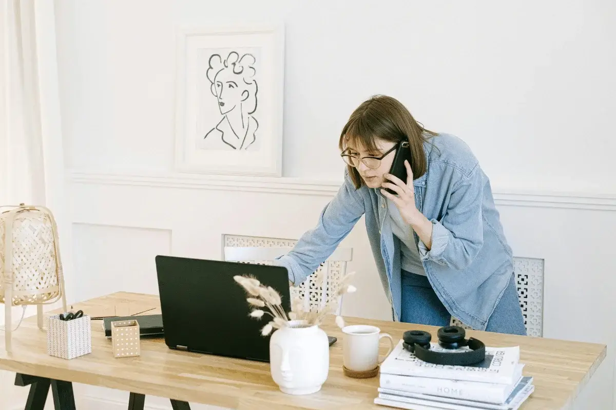 Businesswoman managing remote work, speaking on the phone while leaning over her laptop in a cozy office setup.