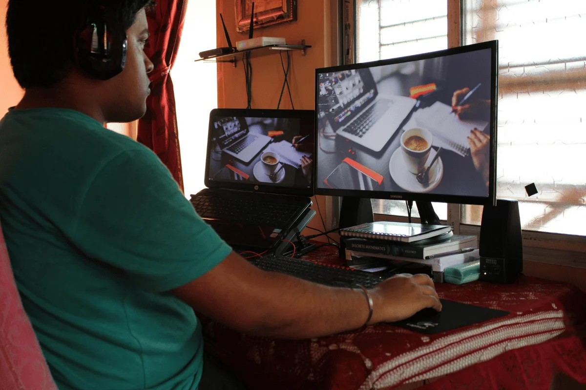 A man wearing headphones working on a dual-monitor setup in a home office with natural lighting.