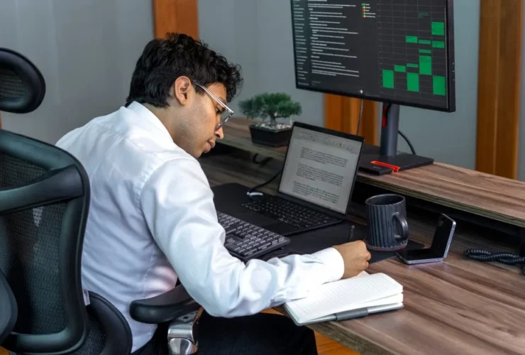 Developer implementing priority scoring system at desk with monitor displaying data analytics dashboard.