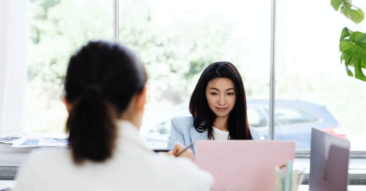 Two professionals discussing priority scoring system at bright office desk with laptop and documents visible.