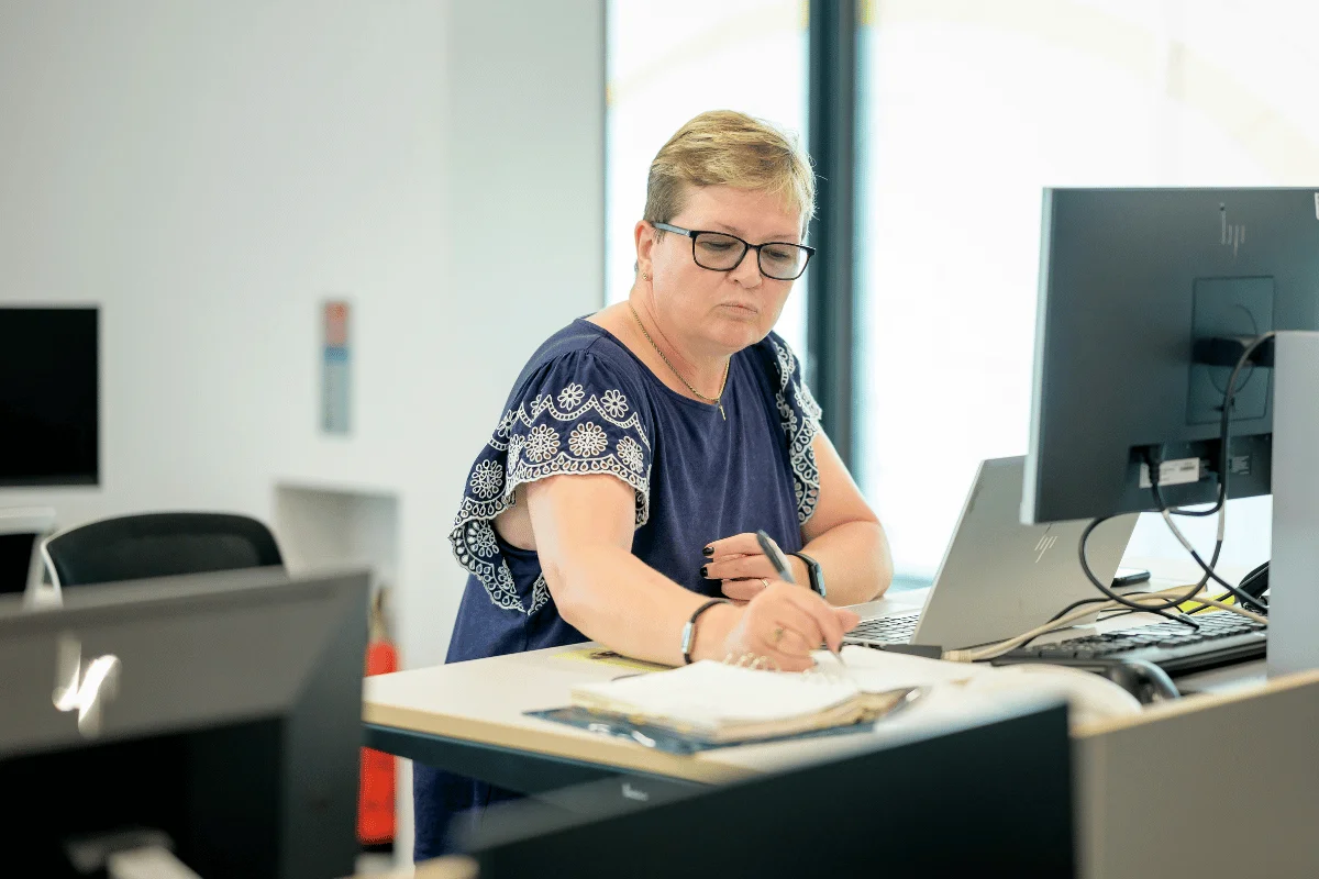 Professional taking notes while using desktop computer.