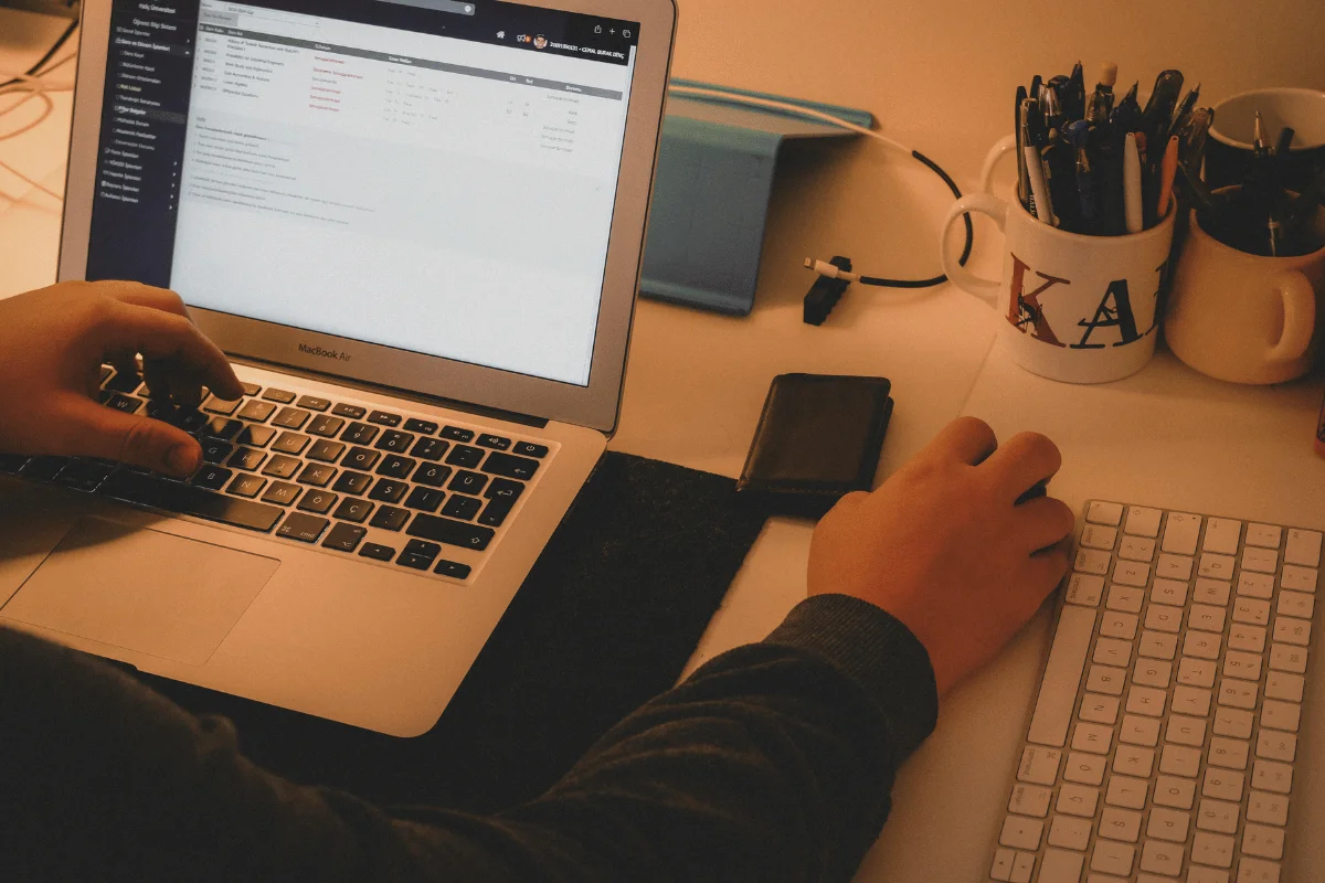 A person works at a cluttered desk, using a laptop and external keyboard.