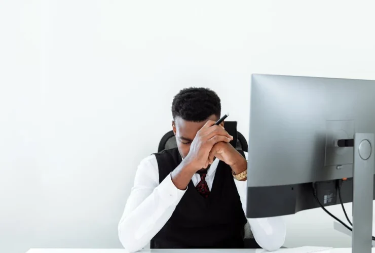 Stressed executive at desk covering face while working on computer, showing outsourced executive assistant red flags.
