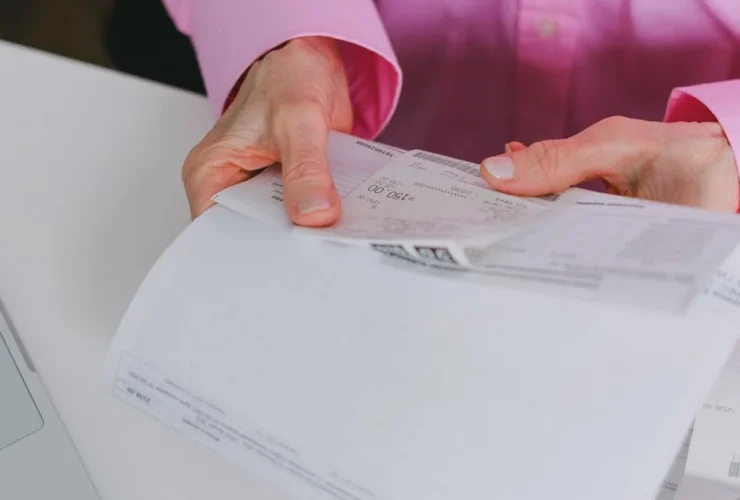 Person in pink shirt opening mail and business documents on white desk.