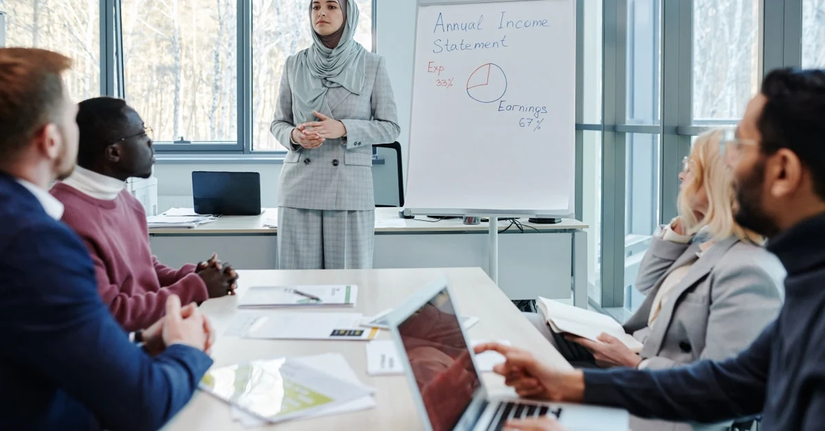 Woman in hijab presenting nonprofit strategy on whiteboard to diverse team in modern office meeting room.