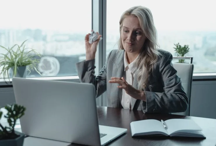 Professional woman on video call at high-rise office desk preparing for investor meetings with laptop and open notebook.