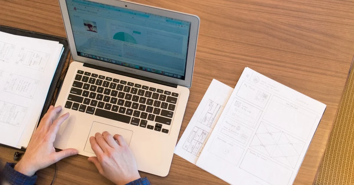 Hands typing on laptop at desk with wireframe sketches and notes for executive assistant fundraising planning.