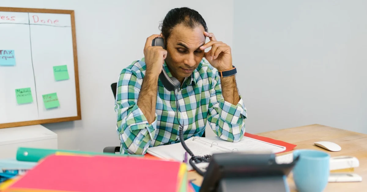 Man in plaid shirt adjusting headphones at desk with colorful notebooks and supplies, representing executive assistant.