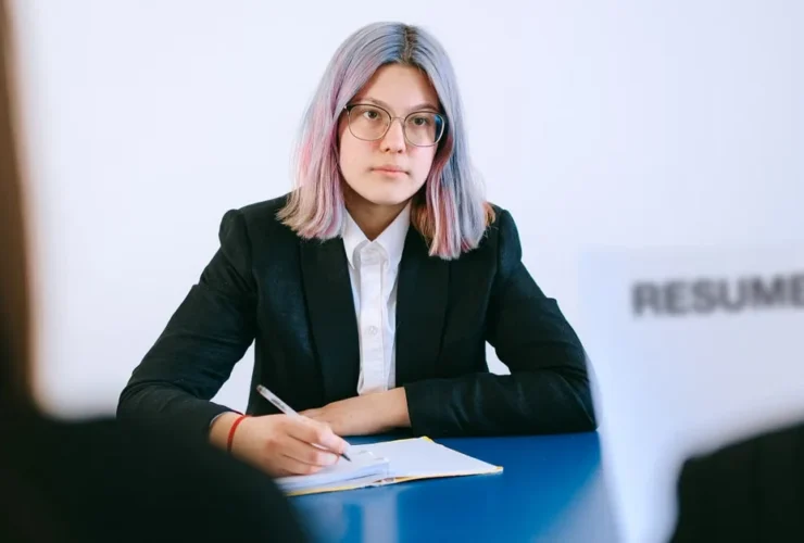 Woman with glasses in black blazer holding resume during job interview, demonstrating virtual assistant skills.