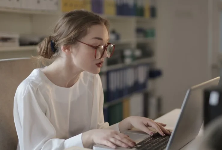 Woman with glasses typing on laptop at desk with notebook, representing virtual assistant nonprofits work environment.