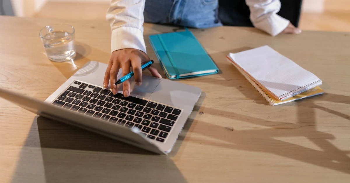 Executive assistant working on laptop at desk with notebooks and water glass during meeting preparation