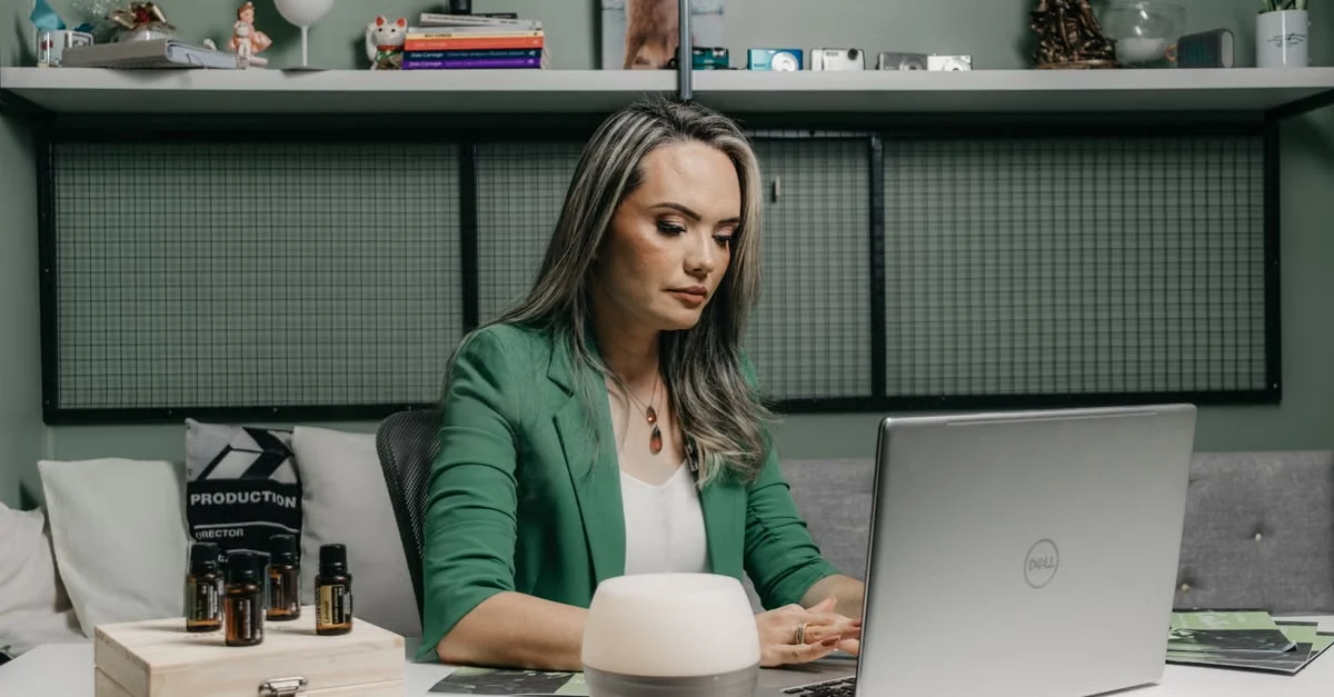Woman with virtual assistant skills working at desk with laptop, humidifier, and organized green shelving.