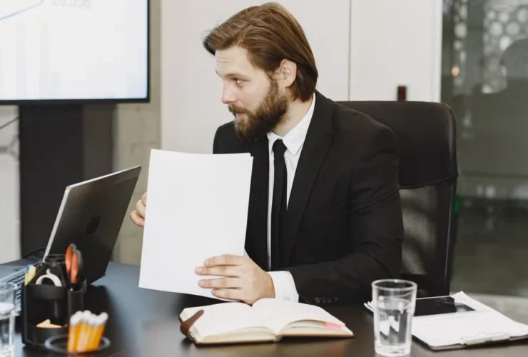 Person typing on laptop at wooden desk with wireframe sketches and documents for executive assistant keynote support.