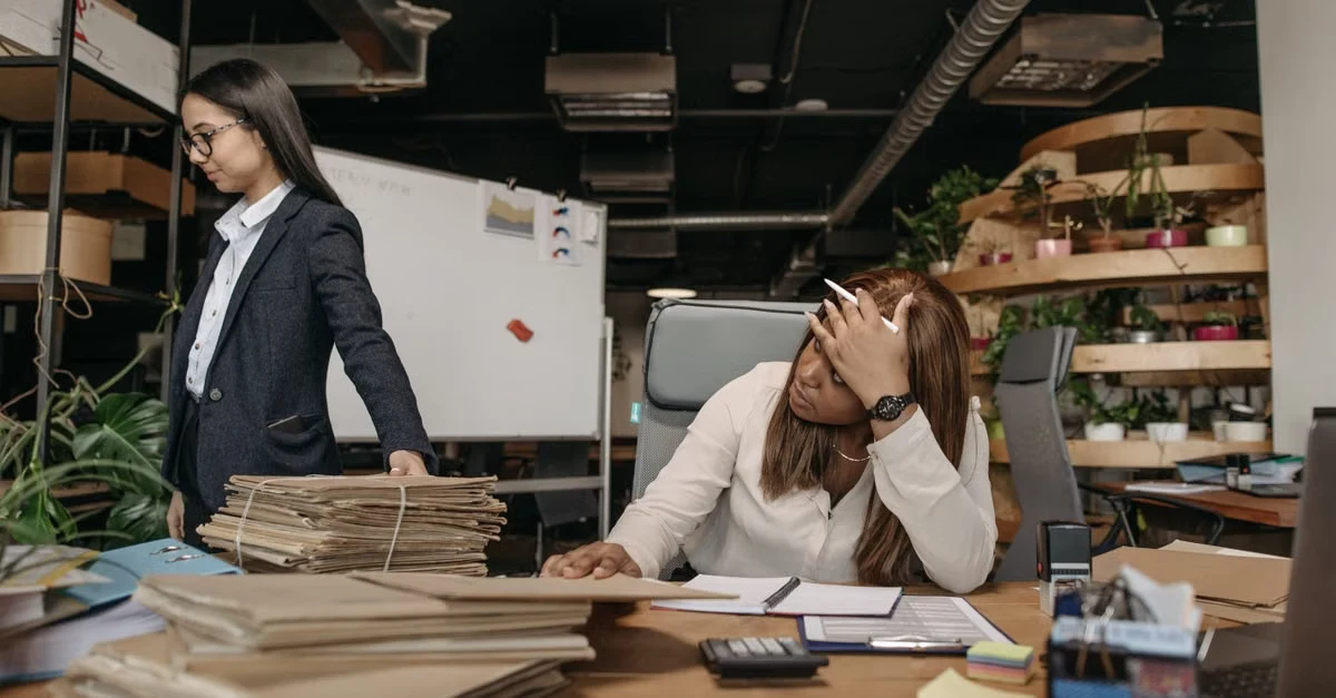 Executive assistant professional boundaries in workplace: woman at desk reviewing documents while colleague stands nearby.