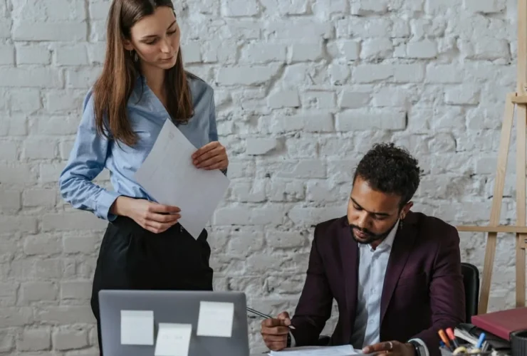 Woman presenting document to seated man at desk in modern office.