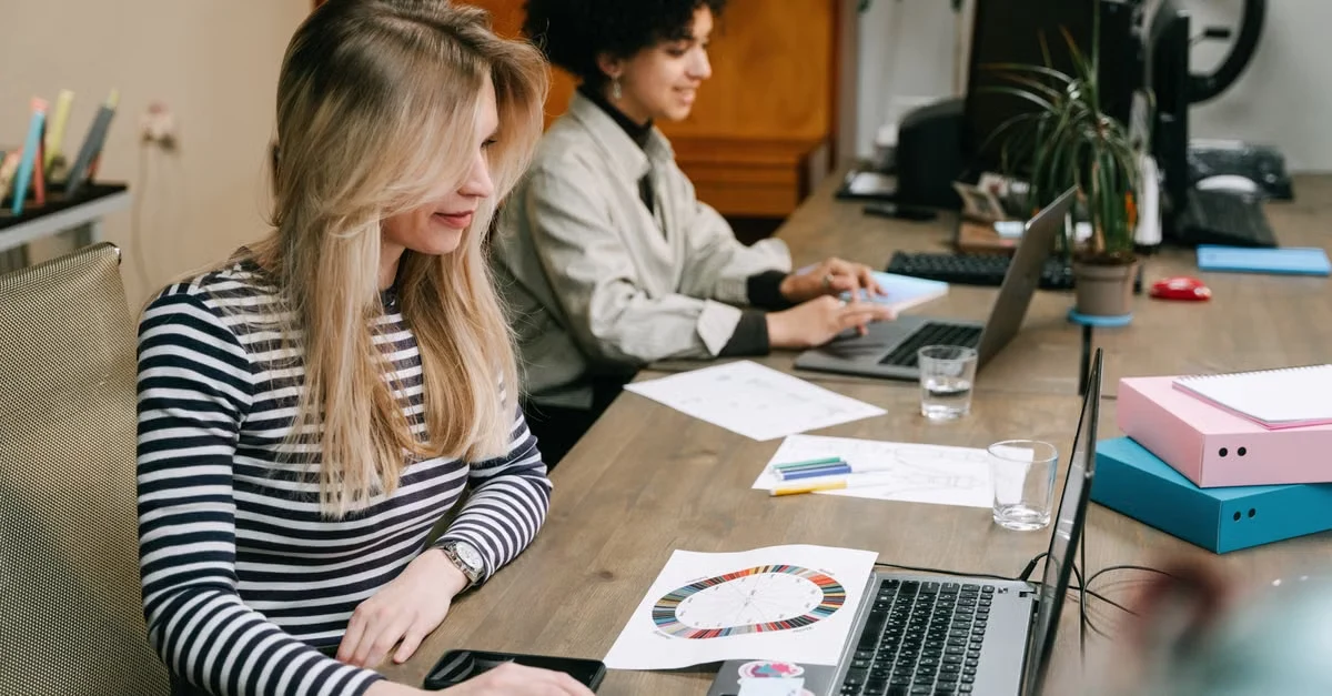 Two professionals working at laptops with documents, comparing Zirtual alternative assistant services in modern office.