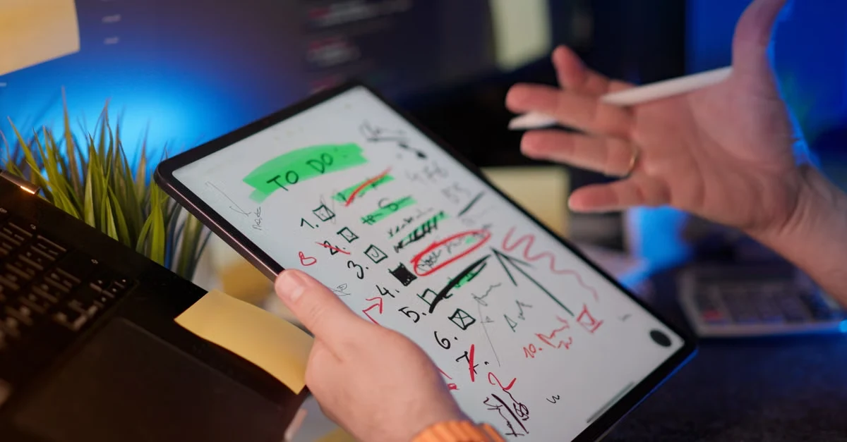 Executive assistant reviewing task notes on digital tablet with handwritten markings and calculations during discussion.