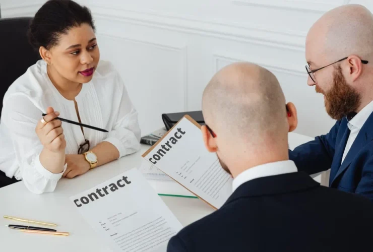 Woman lawyer boldly reviews contract terms with two male business clients at office desk meeting.