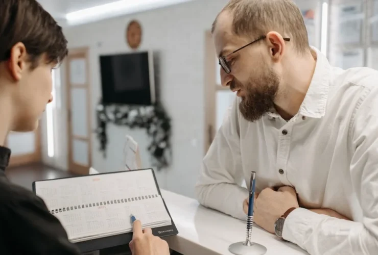Professional man in glasses discussing health coordination notes with female employee at office desk consultation.