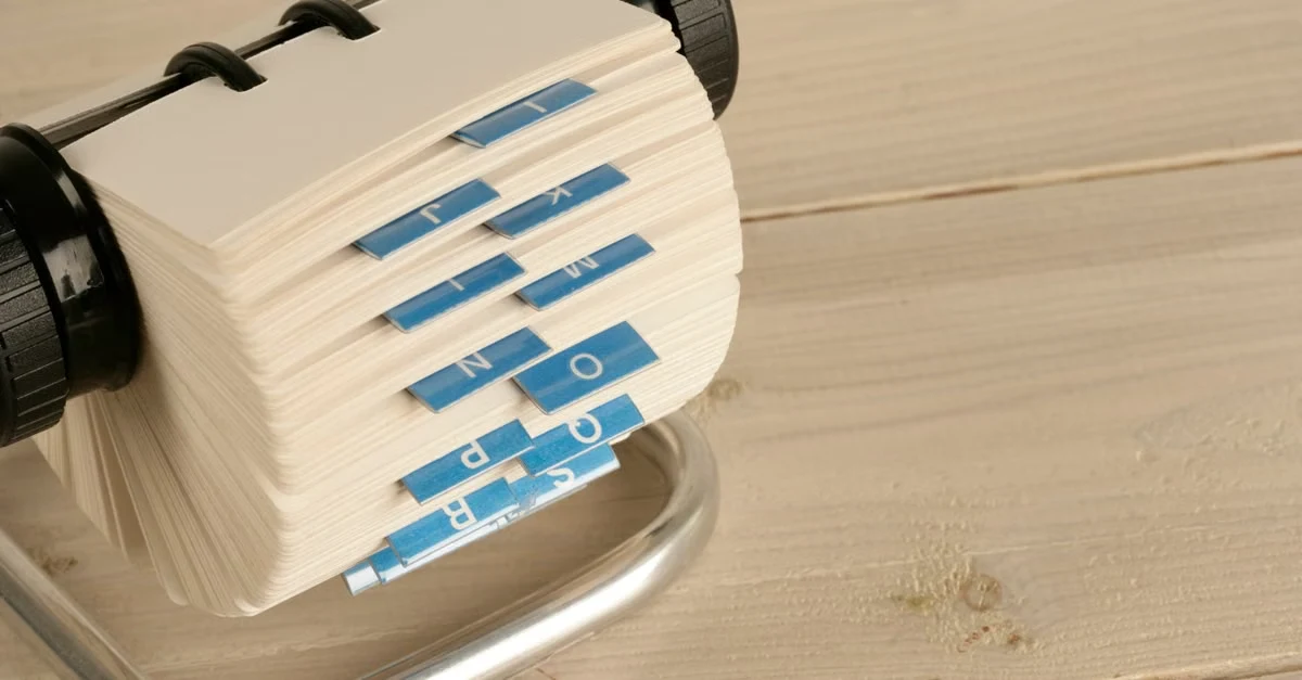 Rolodex with blue contact cards for executive assistant health coordination on wooden desk.