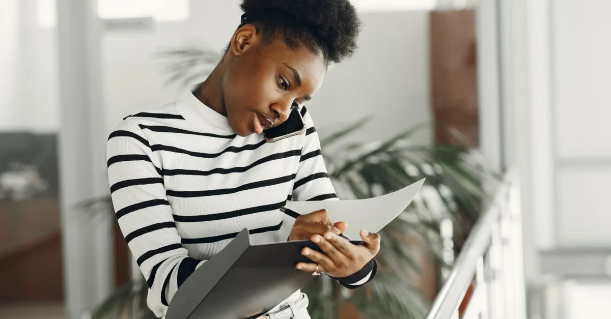 Woman reviewing contact database management notes on tablet while organizing client information in bright office.
