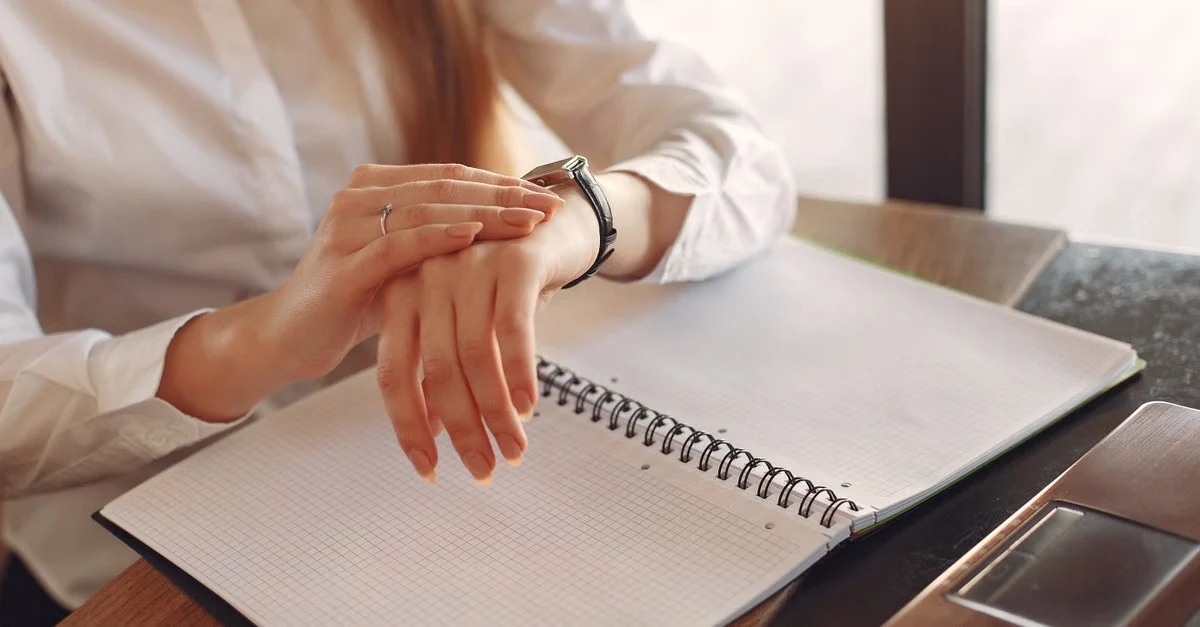 Remote executive assistant time zones: woman in white shirt pointing at blank spiral notebook while managing schedule.