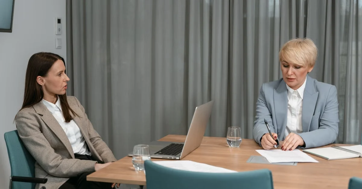 Executive assistant conducting 90 day planning meeting with colleague at conference table with laptop and documents.