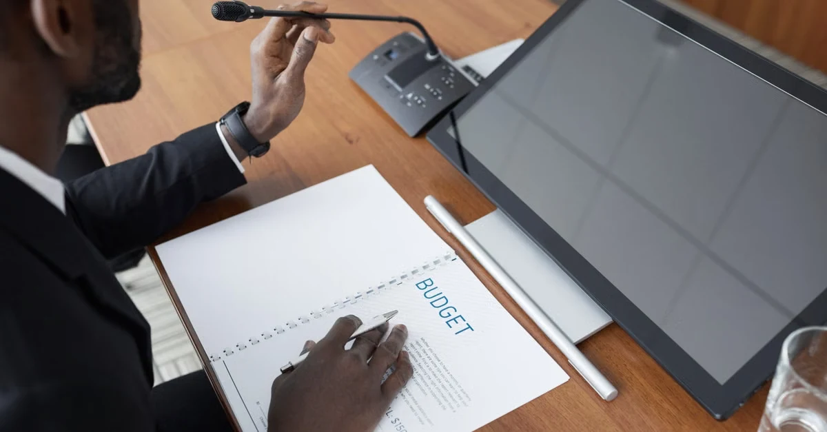 Executive assistant reviewing 90 day planning document with stylus and tablet at wooden desk.