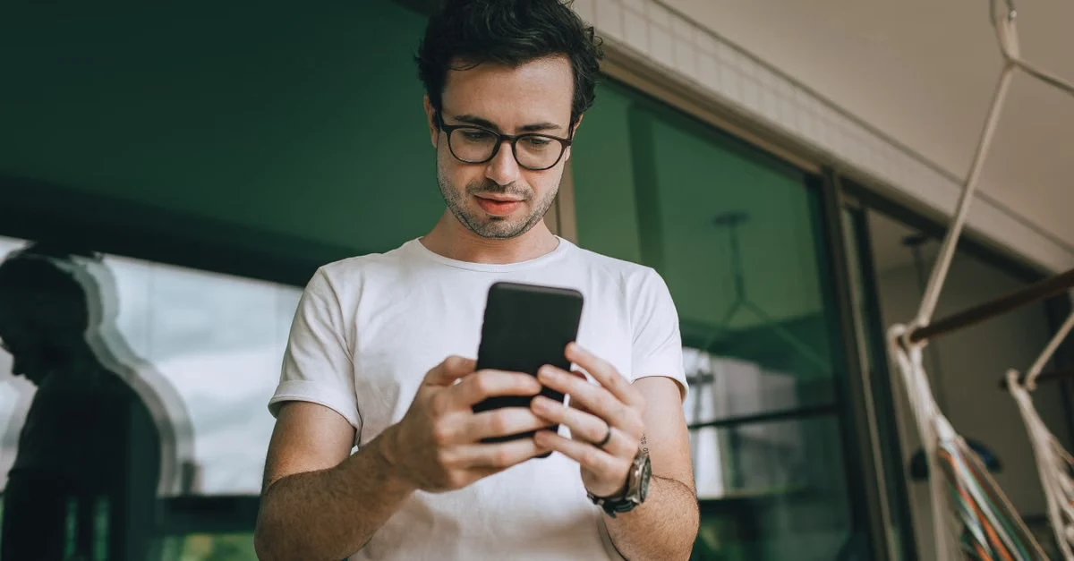Man in glasses holding smartphone while reading Time Etc reviews in modern office space.