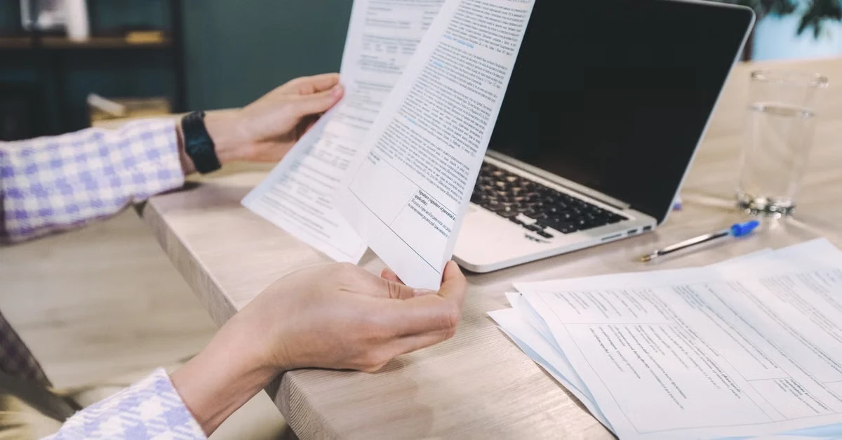 Person reviewing financial documents at desk with laptop and papers for Time Etc reviews analysis.