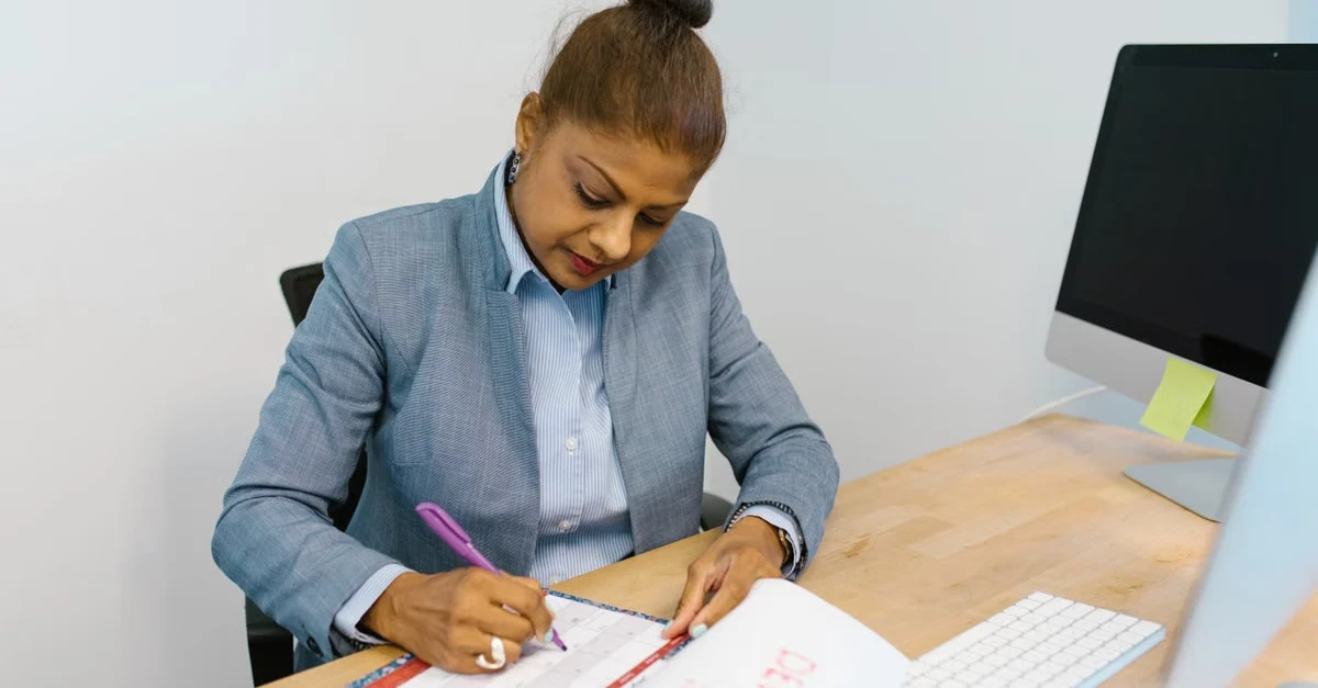 Executive assistant planning quarterly goals using 90 day planning notebook at desk with computer.