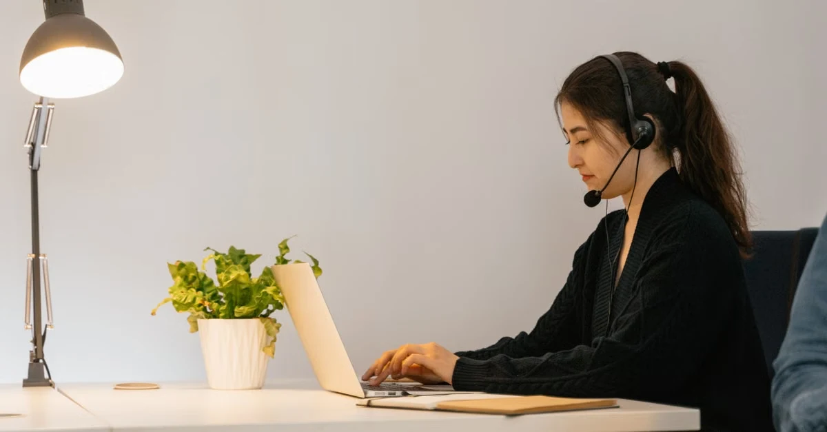 Woman in headset typing at desk with potted plant and lamp, researching boldly reviews alternative.