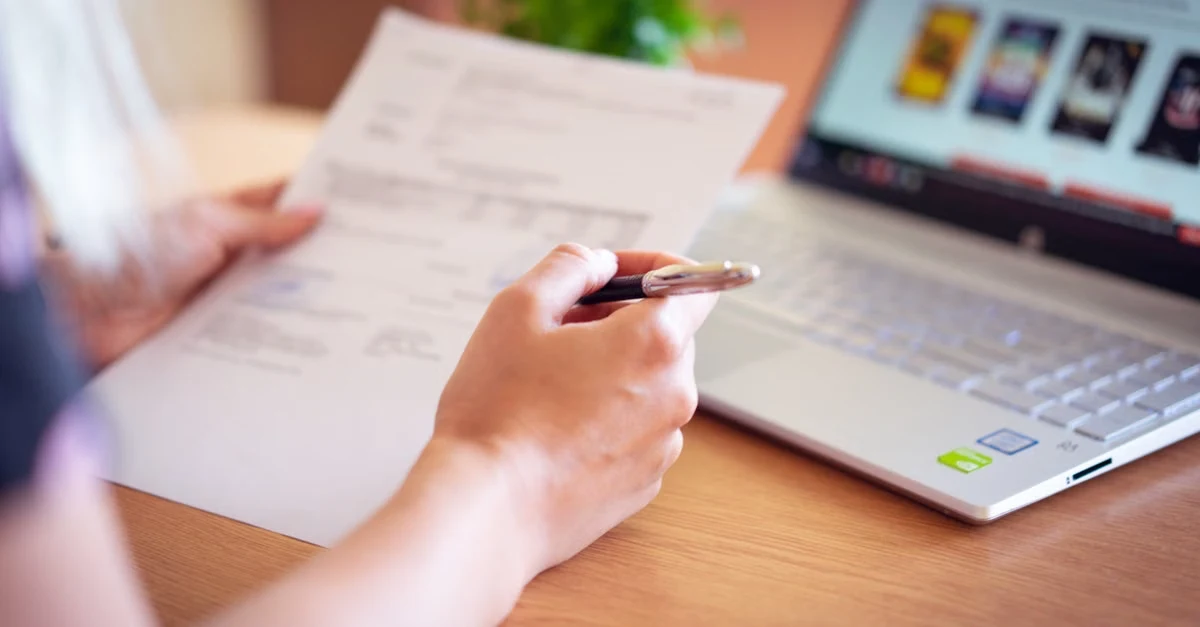 Professional holding pen reviewing Time Etc pricing details on wooden desk with laptop and documents nearby.