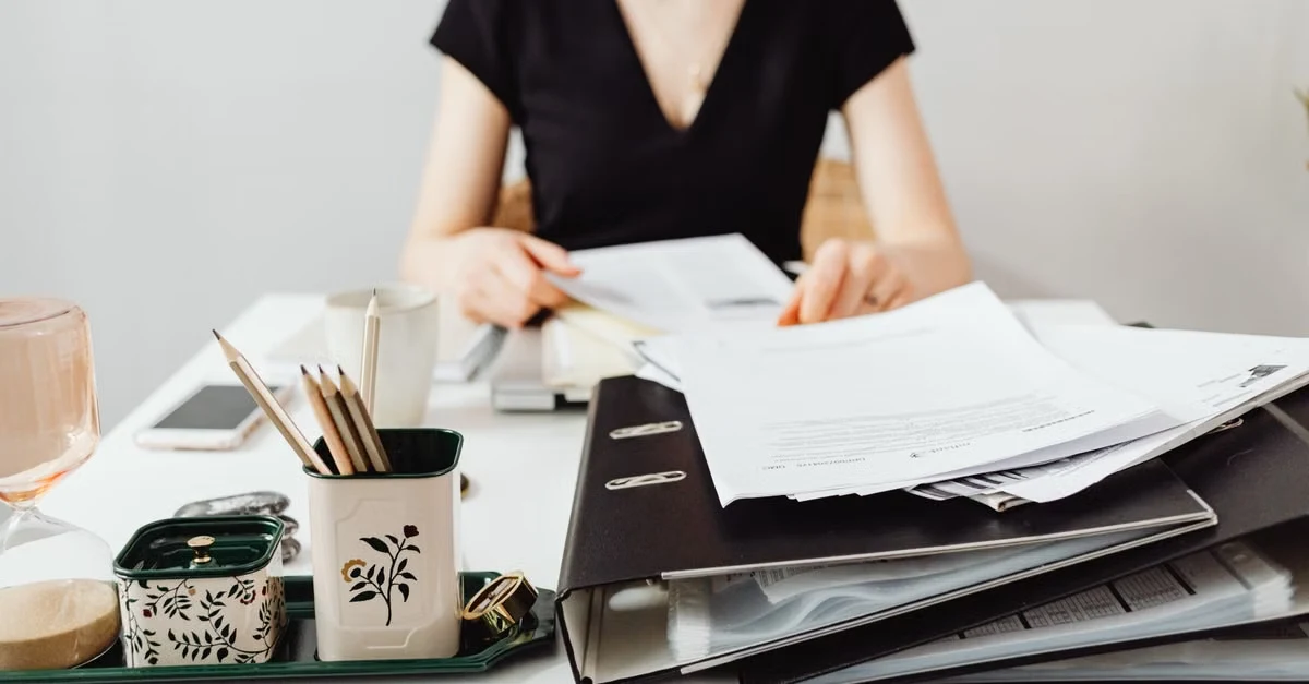 Executive assistant managing health coordination documents and schedules at organized desk with filing system.