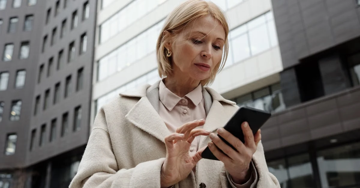 Professional woman reviewing contact database management on mobile device in downtown business district.