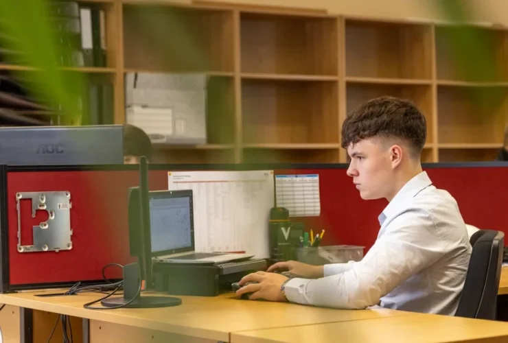Male professional at desk with computer and red office divider, working in modern startup office environment.