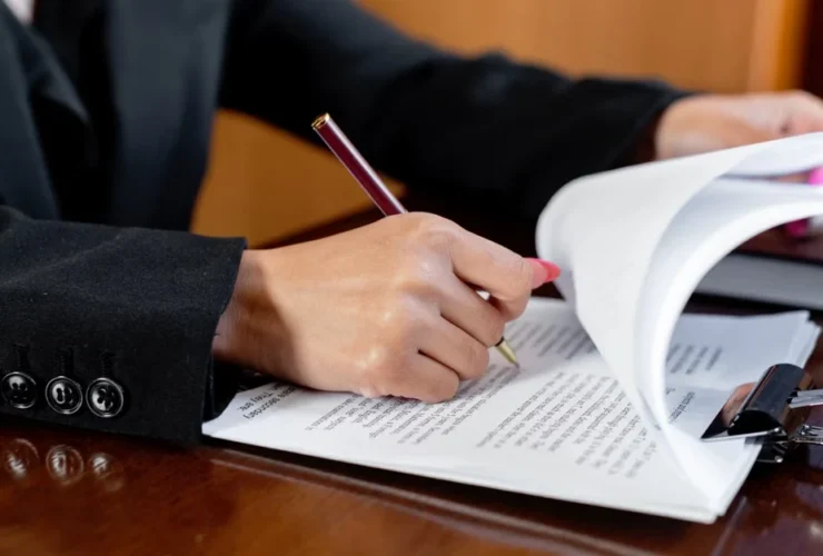 Executive assistant legal compliance professional signing contract document at desk with pen and keys.