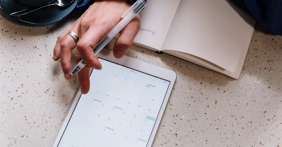 Hand holding stylus over digital calendar on tablet, organizing executive assistant healthcare tasks and schedules.