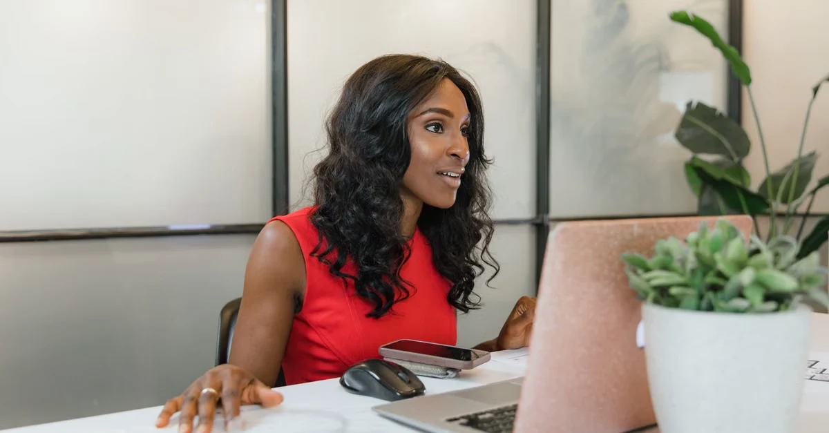 Woman in red top at desk with laptop and potted plant, representing executive assistant startups support roles.