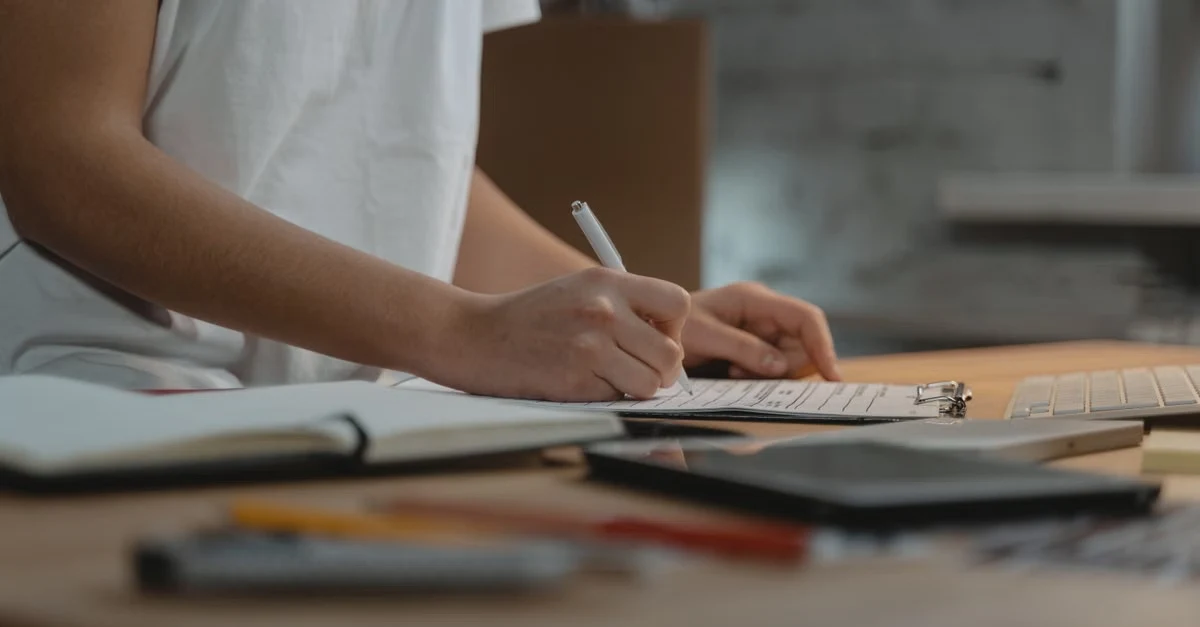 Person writing in executive assistant decision log notebook at desk with planning materials and supplies.