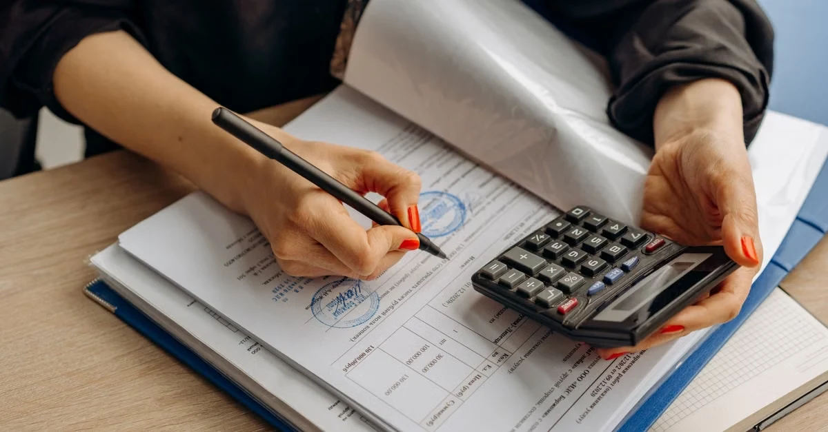 Person reviewing receipts and using calculator for corporate card expense audit verification on wooden desk.