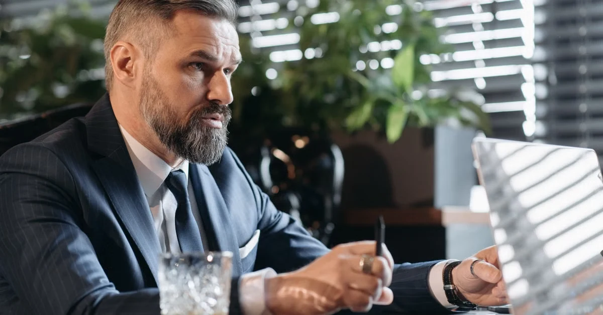 Bearded businessman in suit concentrating at desk during executive assistant startup meeting discussion.