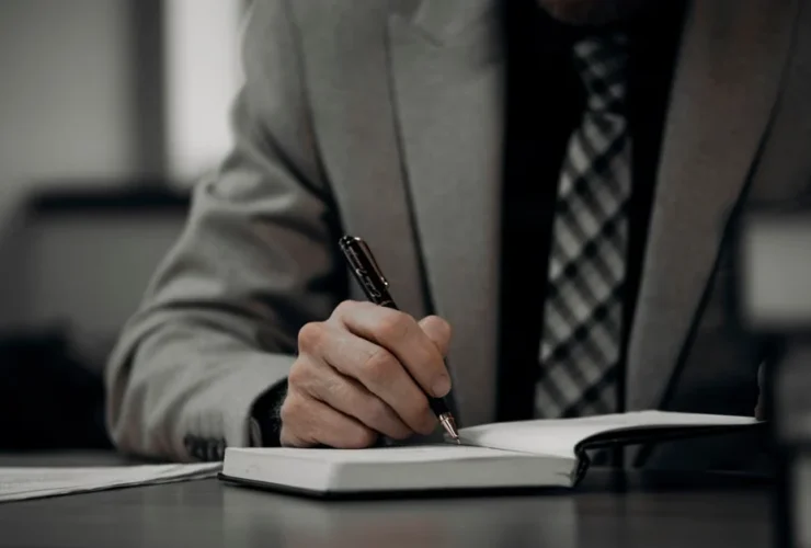 Professional in gray suit signing document at desk, relevant to Wing assistant reviews comparison.